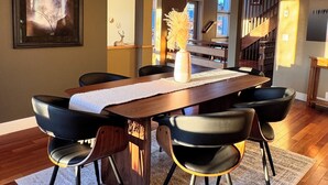 A dining area with a long wooden table, black chairs, a white rug, and a hanging light fixture. - NEW Modern Mountain Haven | Luxe View, Sauna, Hot Tub & Fireplace (Nelson)