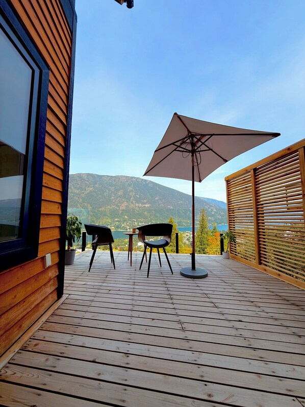 A wooden deck with two chairs and a table, overlooking a mountainous landscape.