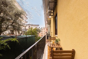 A balcony with a wooden table and chairs, a potted plant, and a view of neighboring buildings. - Charming&Modern One-Bedroom Apartment in Sorrento (Sorrento)