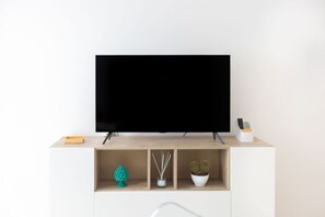 Una sala de estar moderna con un televisor de pantalla plana sobre un mueble de madera, una planta pequeña, un árbol decorativo y un difusor de cañas.