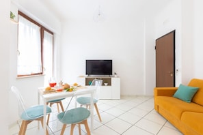 A bright living room with a dining area, a TV on a white cabinet, and a sofa with a cushion. - Charming&Modern One-Bedroom Apartment in Sorrento (Sorrento)