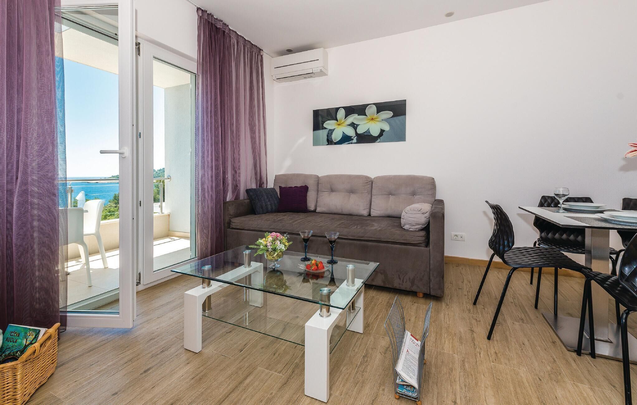 Ein modernes Wohnzimmer mit Glastisch, einer Couch mit Kissen, einem Essbereich mit Tisch und Stühlen sowie Meerblick durch eine Glastür.