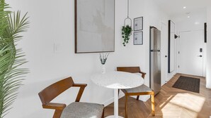 A modern dining area with a round table, two chairs, a hanging plant, and framed certificates on the wall.