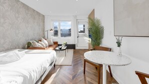 A modern hotel room with a large bed, a small dining table, a sofa, and a potted plant.
