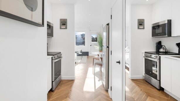 A modern kitchen with white cabinets, stainless steel appliances, and a herringbone wood floor.