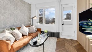 A modern living room with a brown leather sofa, a glass coffee table, and a large window with a view of buildings.