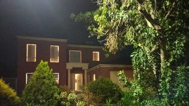 Un edificio de varios pisos con ventanas iluminadas, rodeado de abundante follaje y plantas.