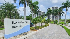 A sign for Bay Harbor Club with a paved walkway and palm trees. - Huge Balcony, Amazing Beach Views & Amenities (Bonita Springs)