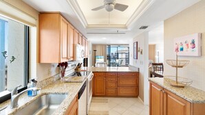 A kitchen with granite countertops, wooden cabinets, a ceiling fan, and a dining area with a view. - Huge Balcony, Amazing Beach Views & Amenities (Bonita Springs)
