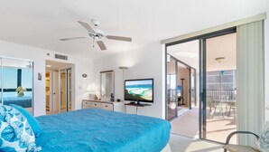 A hotel room with a large bed, a ceiling fan, a TV, and a sliding glass door leading to a balcony with outdoor furniture. - Huge Balcony, Amazing Beach Views & Amenities (Bonita Springs)