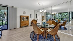 Un espace repas moderne avec une table en verre entourée de chaises en osier, un buffet en bois et un grand miroir qui reflète la pièce.