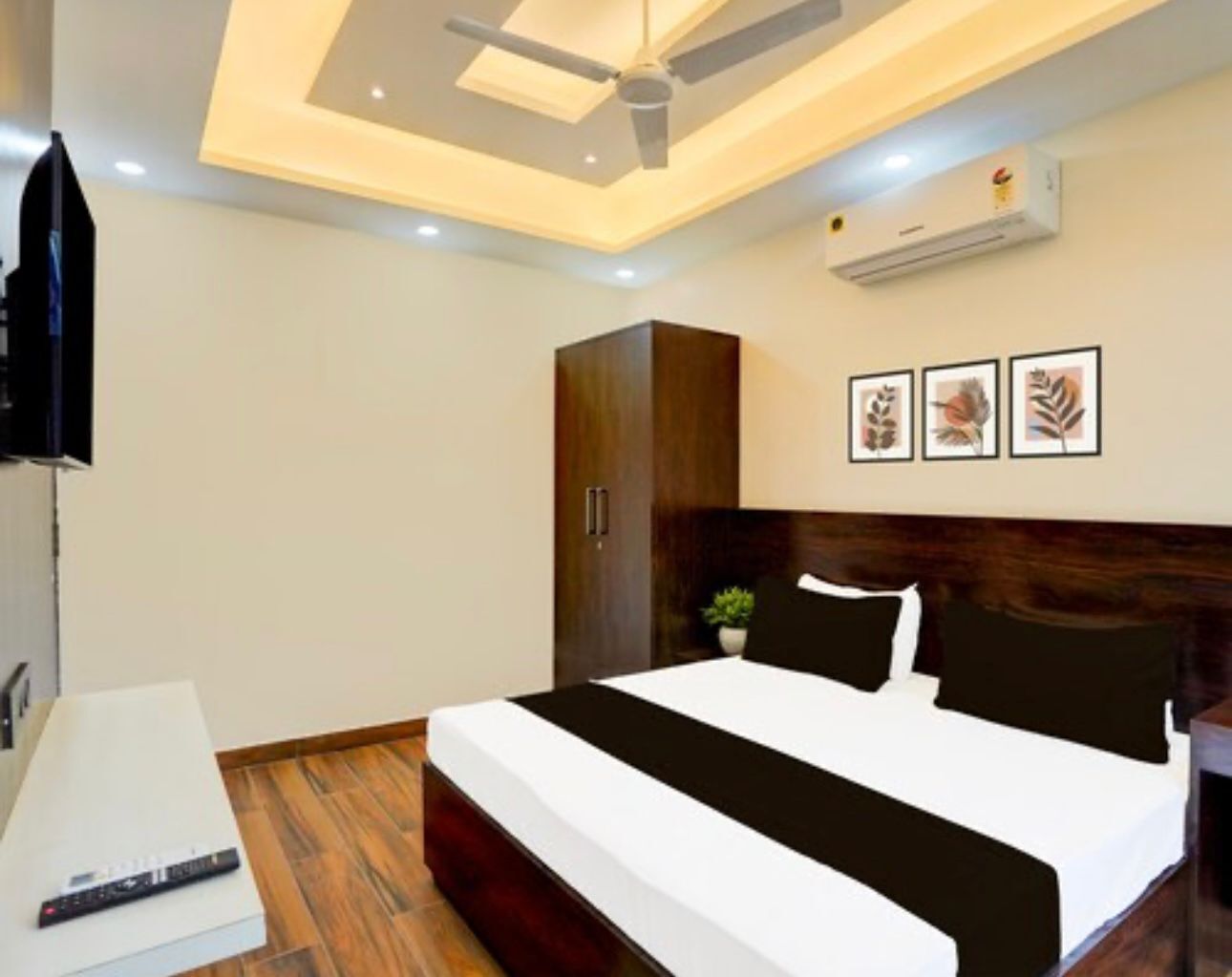 A modern bedroom with a large bed, a ceiling fan, an air conditioner, and framed artwork on the wall.