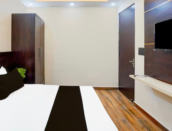 Una habitación de hotel moderna con una cama grande, un armario, un televisor y piso de madera.