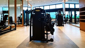 A modern gym with various exercise machines, large windows, and a clean, spacious layout.