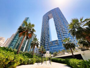 Un moderno edificio de gran altura con un diseño de arco característico, rodeado de exuberante vegetación y palmeras.