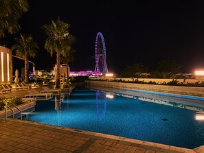 Un área de piscina nocturna con sillones de descanso y palmeras.