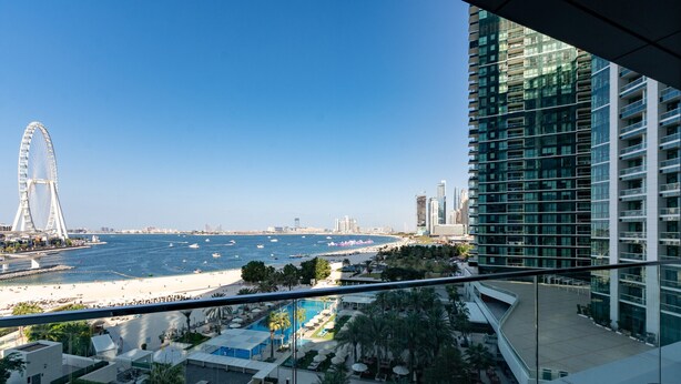 A high-rise hotel with a view of a beach, a Ferris wheel, and a pool area.