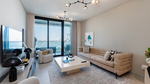 A modern living room with a large window, a beige sofa, a coffee table, and a chandelier.