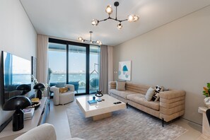 A modern living room with a large window, a beige sofa, a coffee table, and a chandelier.