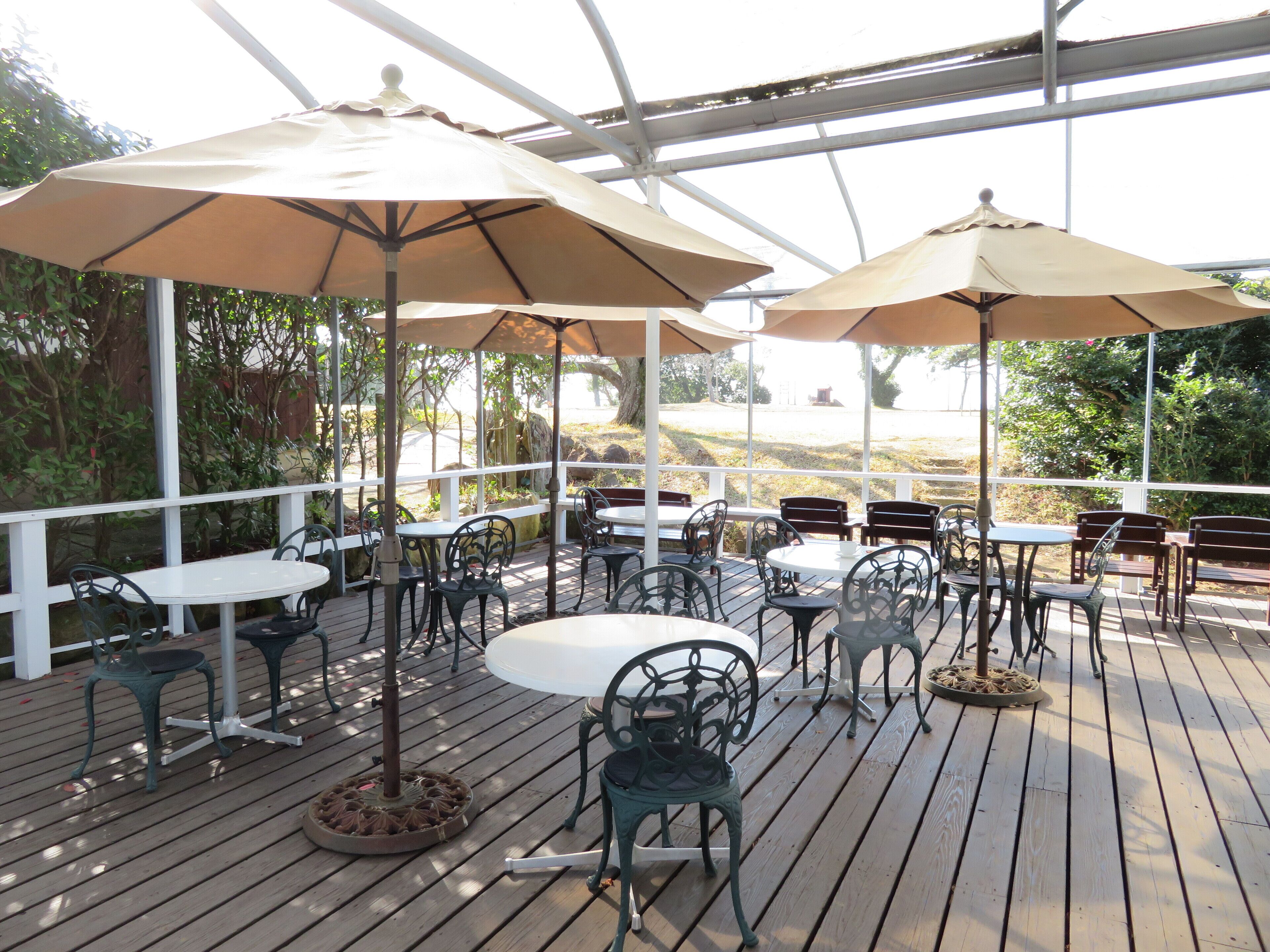Un patio exterior con mesas y sillas, cubierto por grandes sombrillas.