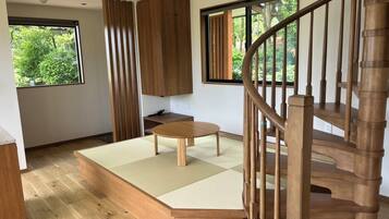 A modern interior with a wooden staircase, a tatami mat seating area, and large windows offering a view of greenery.