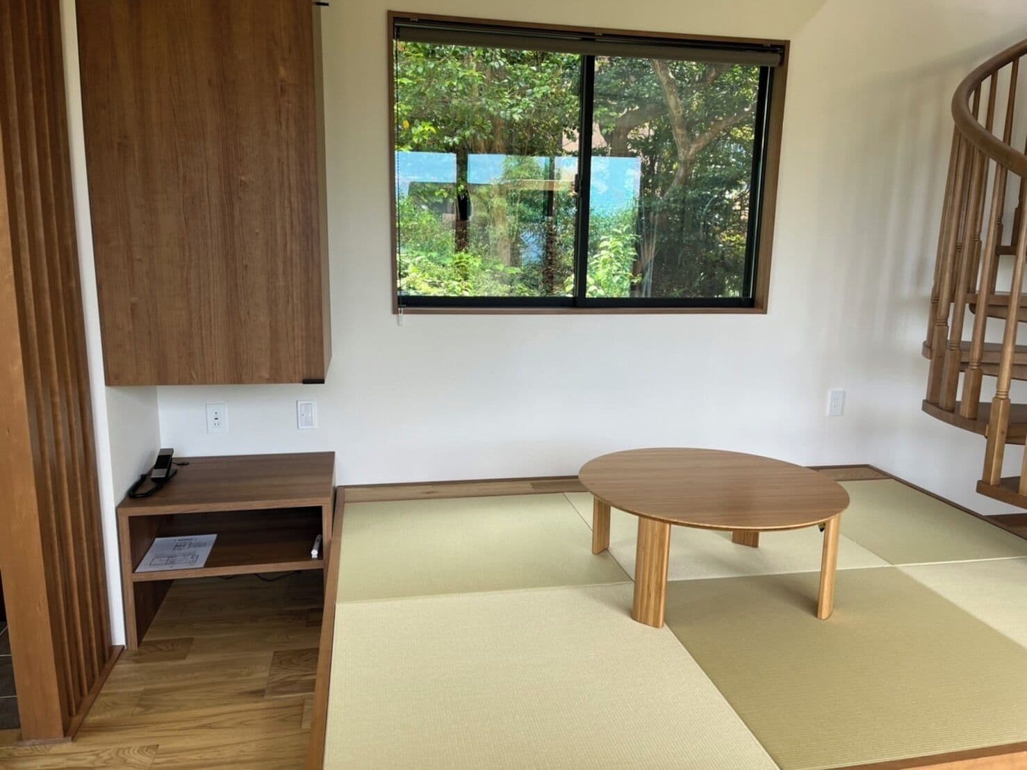 Une pièce avec des tatamis, une table en bois, un meuble et une fenêtre donnant sur un paysage verdoyant.