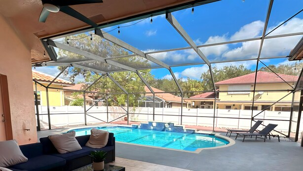Area piscina interna con soffitto in vetro, un divano blu e poltrone relax.