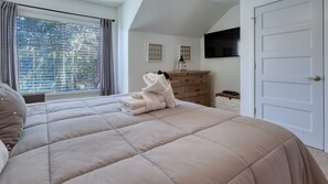 Une chambre avec un grand lit, une commode, un téléviseur fixé au mur et une fenêtre avec des rideaux.