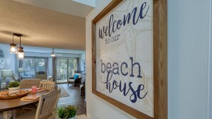 Un comedor con una mesa de madera, sillas y un letrero en la pared que dice 'welcome to our beach house'.