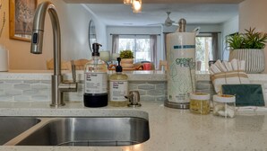 Una cocina con un lavamanos de acero inoxidable, una botella de detergente, una botella de jabón para manos y un dispensador de jabón verde.
