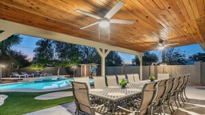 An outdoor patio with a pool, a dining table with chairs, and a ceiling fan.