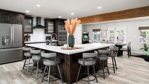 A modern kitchen with a large island, bar stools, a microwave, and a coffee machine.