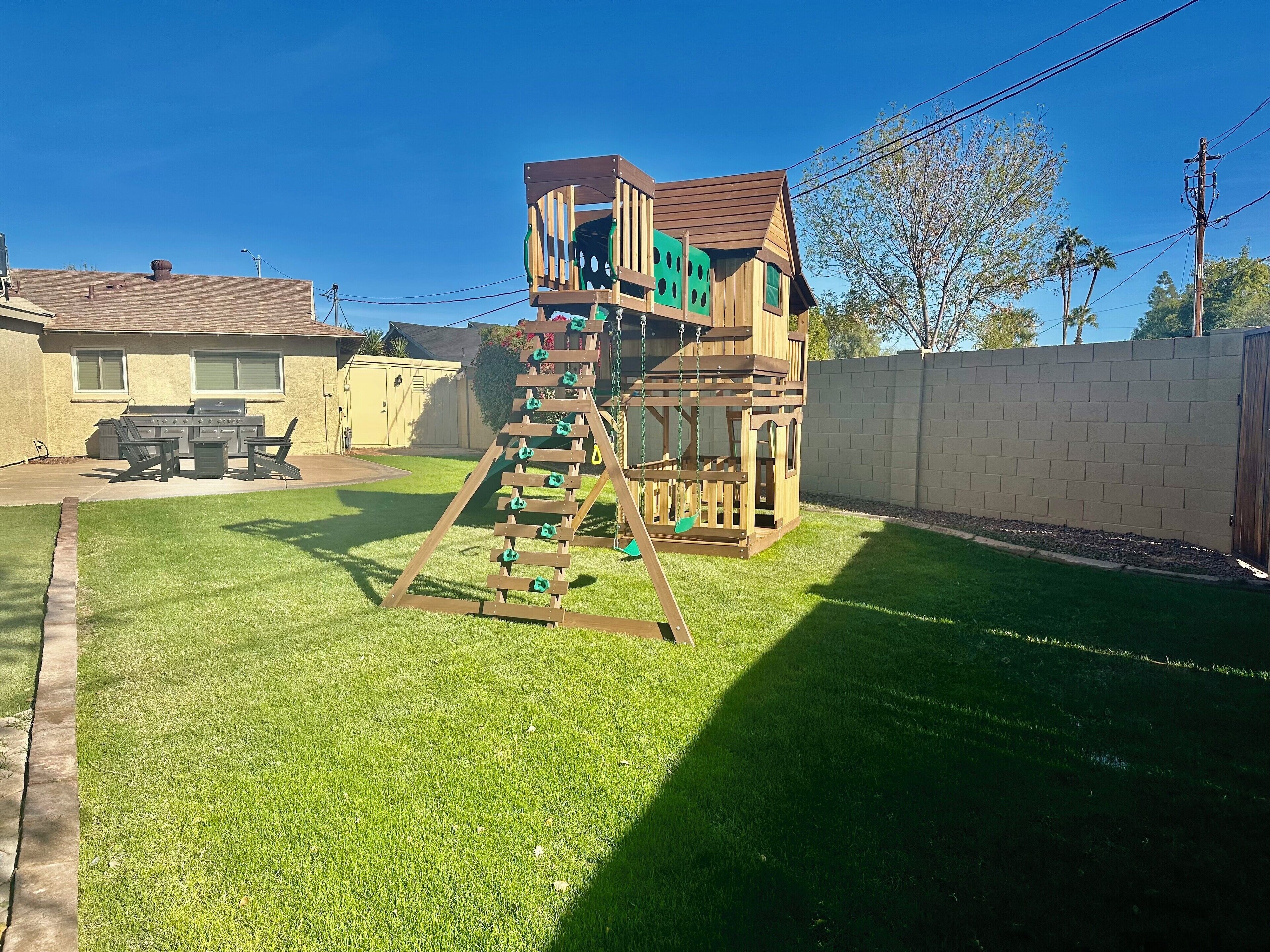 A wooden play structure with a slide and climbing ladder in a backyard.