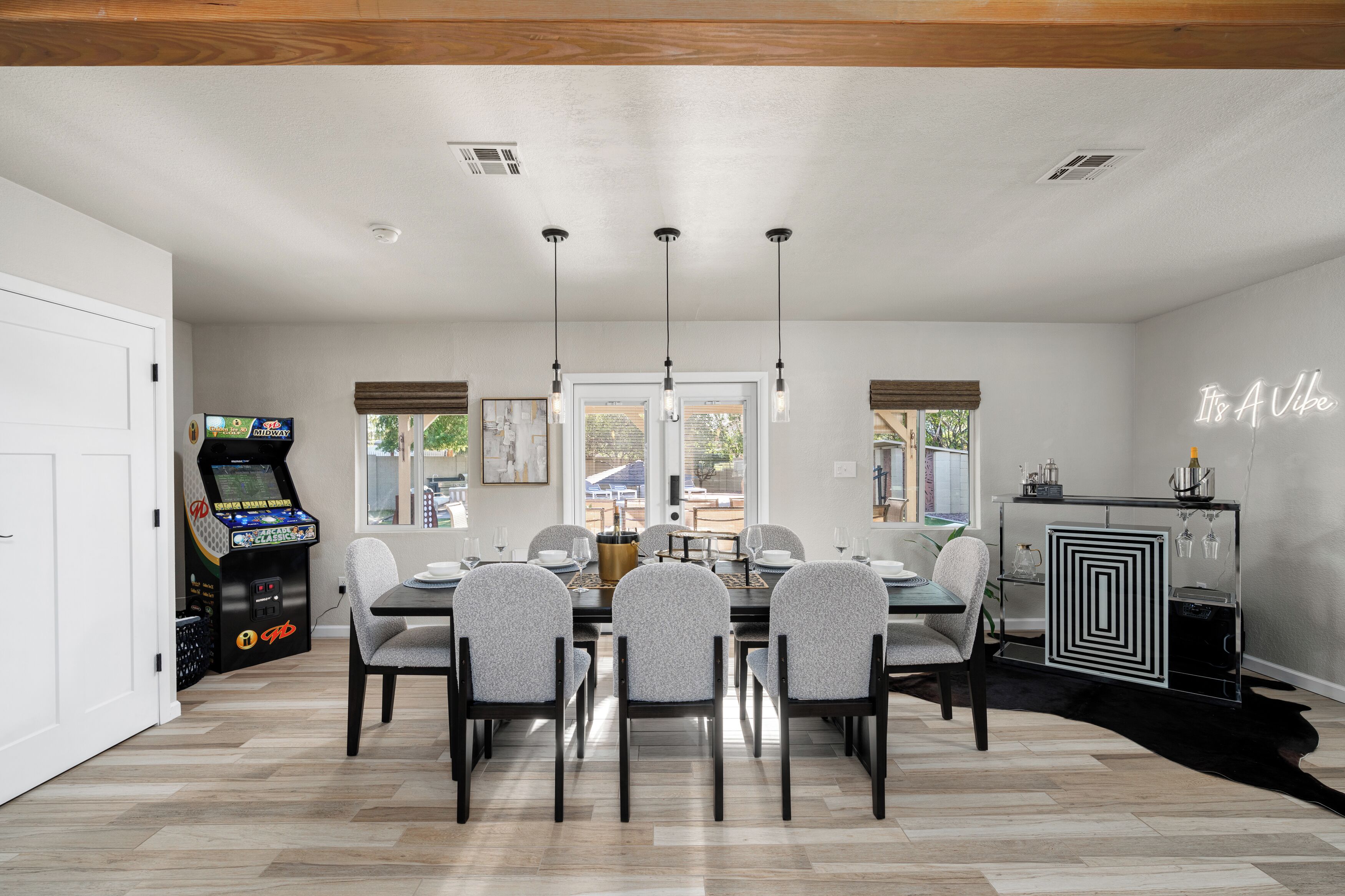 A dining area with a table set for six, a console game, and a neon sign on the wall.