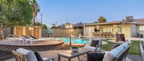 A backyard with a swimming pool, outdoor furniture, and a patio area.