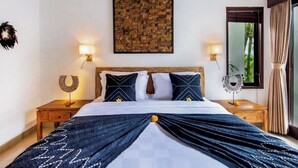 A hotel room with a bed, two bedside tables, a wall-mounted artwork, and a window with curtains. - Villa Joyosa (Seminyak)