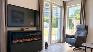 Moderni olohuone, jossa on takka, litteänäyttöinen televisio, mukava nahkainen nojatuoli ja lasiliukuovi, joka johtaa parvekkeelle.