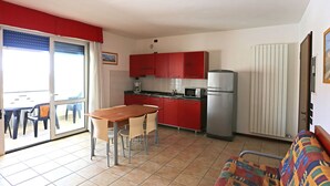 Une cuisine compacte avec des meubles rouges, un réfrigérateur en acier inoxydable et un coin repas comprenant une table et des chaises.