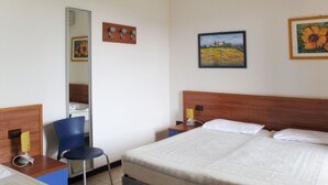 Hotellihuone, jossa on sänky, tuoli, työpöytä, peili ja taulu seinällä.
