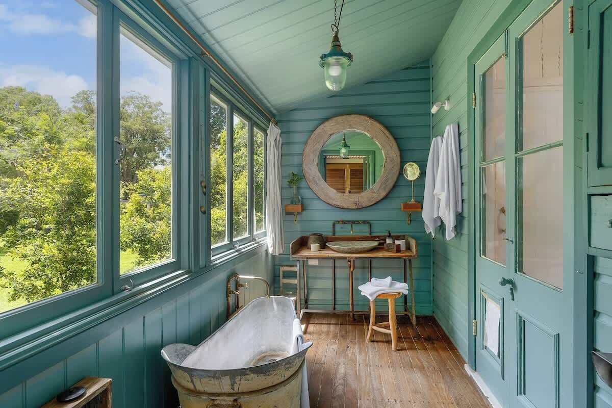 A character-filled bathroom with a freestanding clawfoot bath, timber floors and leafy garden views. A peaceful space to slow down, soak and enjoy the charm of this historic Bangalow holiday home.