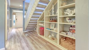 Un escalier en bois recouvert d’une moquette à rayures, une bibliothèque décorée de motifs marins et une porte au fond du couloir.