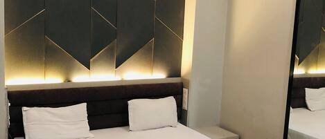 Una habitación de hotel moderna con una cama grande, un cabecero con diseños geométricos, un equipo de aire acondicionado y un espejo.
