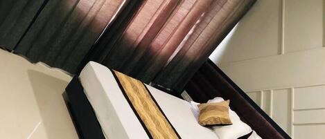 Un lit avec une tête de lit sombre, une literie blanche et deux oreillers.