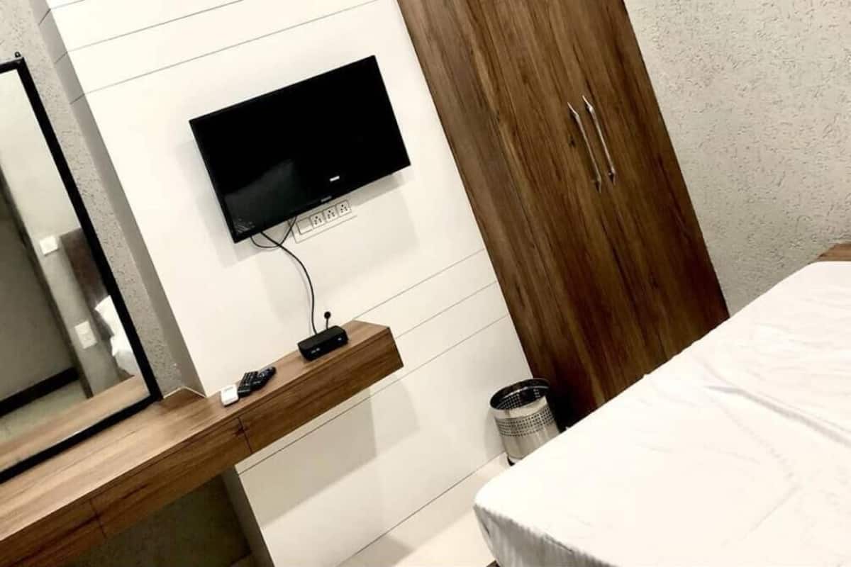 Ein Schlafzimmer mit einem Bett, einem an der Wand befestigten Fernseher, einem Holzschrank und einem kleinen Schreibtisch mit Spiegel.