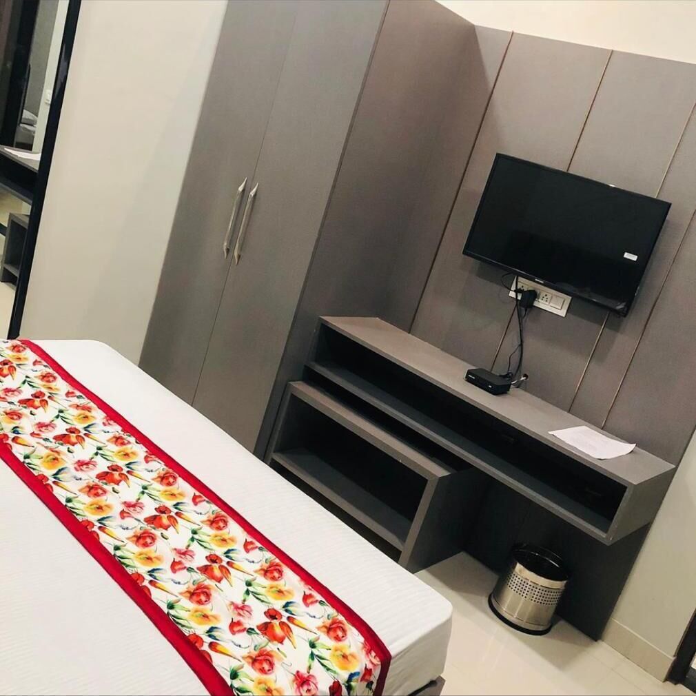 A bedroom with a bed, a TV mounted on the wall, a small desk, and a trash can.