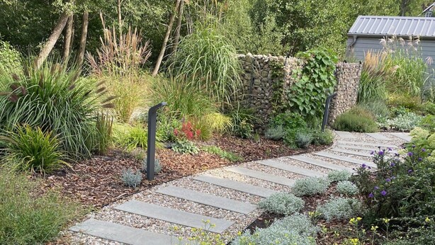 A garden pathway with stepping stones, surrounded by various plants and a stone wall. - Holiday Home by Lake Wiselka & Baltic Beach (gmina Wolin)