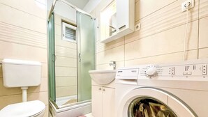 A compact bathroom with a toilet, a washing machine, a sink, and a shower enclosure.