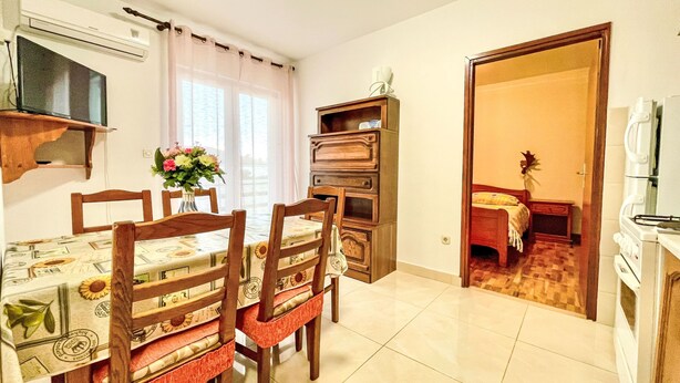 A dining area with a table and chairs, a built-in oven, and a view into a bedroom.