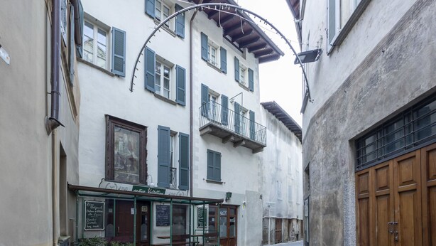 A narrow cobblestone street with a building featuring a cafe with outdoor seating and a signboard listing menu items. - Vicolo Ninguarda by Interhome (Valtellina)