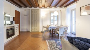 A kitchen with white cabinets, a microwave, and a stove. There is a dining area with a table and chairs, a rug, and a sofa. - Vicolo Ninguarda by Interhome (Valtellina)